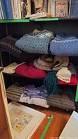 Three folded sweaters on top shelf, middle shelf with red sweater, hat and scarves, bottom shelf with two sweaters