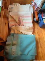 Photo showing four folded wool blankets stacked with pastel striped and beige blankets on top and light blue blanket with satin trim at bottom.