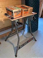 Black & Decker Workmate with two boxes of nails on top, in a storage area with gray flooring and wooden walls.