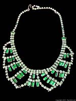 Full view of the vintage bib necklace showing clear and green rhinestones against black background.
