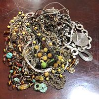 Photo showing tangled assortment of necklaces and jewelry on wooden surface.