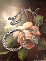 Photo showing the silver bracelet marked Italy 925 and the religious pendant on chain laid flat on a floral surface.