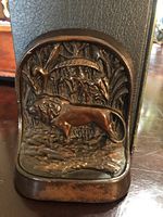 Close-up of one bronze iron bookend showing detailed lion relief and foliage background, exhibiting patina and wear.