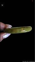Side view of a green marbled Bakelite bangle bracelet held between fingers showing thickness and glossy finish.