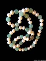 Close-up of the necklace showing alternating white pearls and green jade beads along with a decorative metal clasp.