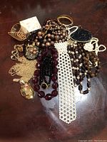 Photo showing a mixed collection of vintage costume jewelry pieces including various bracelets, necklaces, a brooch, earrings, and a mother of pearl jewelry case with gold tone edges on a dark wooden surface.