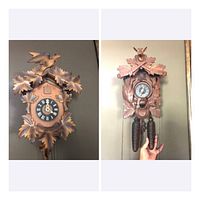 Two wood-carved cuckoo clocks shown mounted on wall. One has bird and maple leaf design, the other deer and oak leaf design, both with weights.