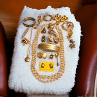 Photo of assorted vintage gold tone costume jewelry laid out on a white textured surface showing necklaces, brooches, rings, earrings, and a decorative barrette.