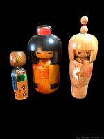 Lot showing three Japanese Kokeshi dolls together on black background. Varied sizes, hair styles, and painted kimono details visible.