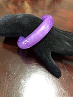 Photo of a solid lavender jade bangle displayed on a black velvet hand mannequin revealing the color and polished finish.