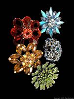 Five vintage floral rhinestone brooches positioned on black background, showing variety of colors and designs.