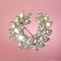 Front view of Sherman brooch showing clear Swarovski crystals arranged in wreath pattern on pink background.