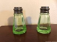 Two uranium glass salt and pepper shakers with sterling silver tops, shown on wooden surface in natural light.