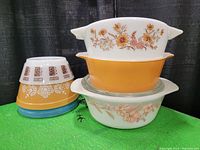 Front view of six bowls and casserole dishes stacked and arranged on a green surface showing patterns and colors.