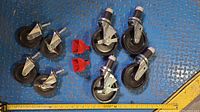 Eight castor wheels including two locking wheels paired with two red metal cowbells placed on blue floor