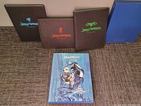 Top-down view of 4 books showing black sketchbooks and one illustrated art book front