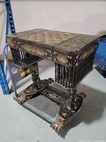 Overall view of table showing black lacquer finish, gold painted scenes, integrated chessboard on top, carved claw feet and spindle supports.