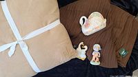 Close-up of one beige Ralph Lauren pillow, two brown Roots knit blankets, and three ceramic figurines including swan, goose, and boy