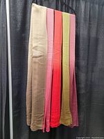 Five extra long scarves hanging together showing their full length and ombre color fade design in sand, pink, red, green and burgundy colors.