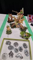 Overview of fairy garden figurines displayed on a white surface with moss accents and the green box with metal collectible gift trinkets in the foreground.