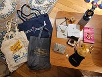 Photo of all items in the lot on wooden floor and table showing tote bags, watch, necklaces, pin, and pouches