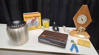 Mixed lot setup including the coffee canister, Curious George glass and book, vintage radio, and trophy clock with small pins and ribbon.
