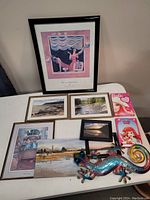 Framed Alberto Morocco print along with six other framed prints, two Barbie valentine cards, and a colorful metal gecko hung or displayed on a surface