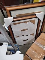 Two wood frames with attached white foldable ULINE protective corners, leaning against a wooden cabinet and boxes.