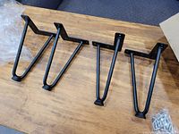 Four black metal hairpin legs, 8 inch height, laid out on a wooden surface with mounting screws and packaging visible.