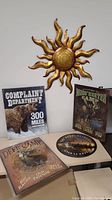 Celestial sun-shaped metal wall decor hanging above four metal signs with wildlife and outdoor themes arranged on table.