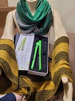 Photo showing neon green hair straightener in box and mannequin wearing green/pink infinity scarf and deep mustard/black infinity scarf on arms.