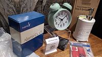 Light mint green alarm clock next to its box, ceramic soap pump with sponge and Toronto Raptors gaiter scarf on acrylic display stand.