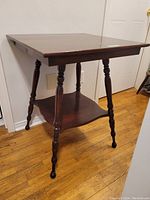 Wooden side table showing side view with turned legs and lower shelf.