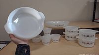 Photo showing large round baking dish held in hand with other dishes and bowls on table.