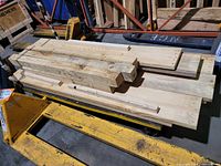 Photo showing a bundle of used wooden lumber pieces stacked on a yellow hand pallet truck, including thick beams and planks.