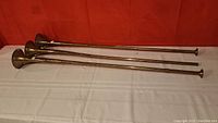 Three brass trumpets laying parallel on a white cloth. Visible length and shape, with flared bell ends.