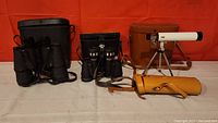 Overall view showing all binoculars, telescope, and carrying cases.