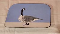 Full view of copper plaque with enamelware art of Canada goose on blue background, showing shape and colors.