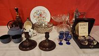 Wide shot of the lot showing tea set cups and pot, floral plate, glass bowl, decanters, blue goblets, candlesticks, and crystal pepper mill and shaker set.