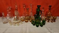 Full view of all decanters and various matching glasses arranged on a table, showing multiple glass sets in amber, green, and clear glass.