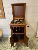 Full view of oak cabinet phonograph with lid open, front storage shelves and lower doors open, crank handle visible