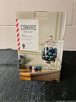 Photo of the front of the Canvas Holiday apothecary jar box showing a filled apothecary jar with holiday ornaments inside.