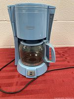 Full view of the blue Betty Crocker coffee maker showing the body, glass carafe, handle, and power cord.