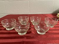 Six clear glass dessert bowls arranged on a red cloth background showing the full set.