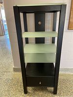 Front view of black wooden frame entertainment shelf with frosted glass shelves and bottom drawer.