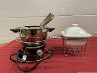 Full view of the fondue pot, dip warmer, and forks on a red surface.