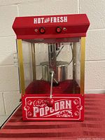 Front view of the red popcorn machine with controls and popcorn graphics, showing the inside kettle and handle.