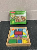 Set includes a wooden train puzzle with colorful geometric shapes and a dinosaur floor puzzle box showing prehistoric dinosaurs and indicating 48 pieces.