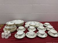 Full set displayed on burgundy tablecloth including plates, cups, saucers, and salt and pepper shakers.
