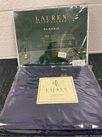 Two sealed Ralph Lauren flat sheets. One package dark green, labeled Lauren Ralph Lauren Classic, 350 thread count, twin flat sheet. The other package navy blue with label saying Lauren Ralph Lauren Classic Sheet 350 thread count, size full flat sheet.